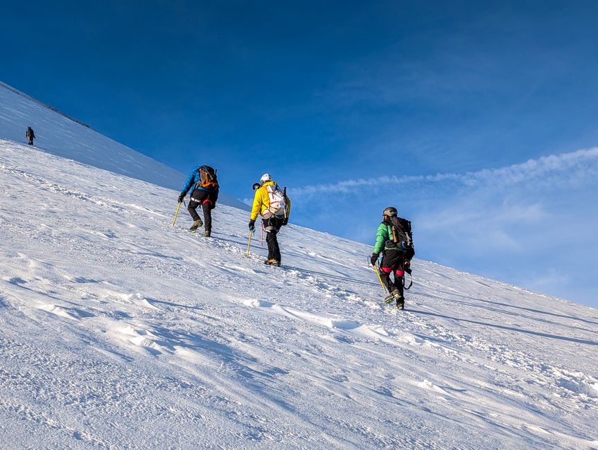 Three climbers ascend a snow-covered slope with ice axes under a sunny blue sky. Perfect for adventure themes.
